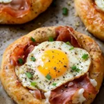 Baked bagels topped with prosciutto, cheese, and eggs on a wooden board