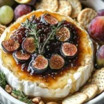 Baked Brie topped with fig jam and fresh rosemary on a wooden serving board.