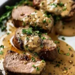 Beef tenderloin with creamy gravy garnished with fresh herbs on a plate.