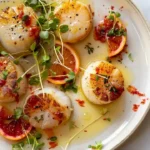 Citrus-marinated seared scallops on a plate, garnished with fresh herbs.