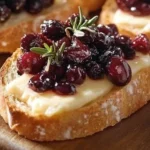 Crostini topped with balsamic roasted cranberries and creamy brie cheese on a plate.