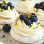 Mini pavlovas with cream, blueberries, and pistachios on a decorative plate