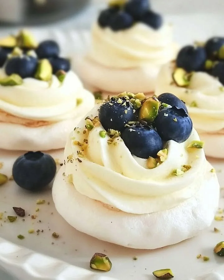 Mini pavlovas with cream, blueberries, and pistachios on a decorative plate