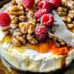 Raspberry and Walnut Baked Brie served on a wooden board with fresh fruit