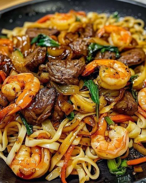Delicious Steak & Shrimp Stir-Fried Noodles garnished with fresh vegetables