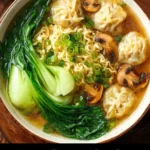 Bowl of wonton noodle soup with mushrooms garnished with green onions
