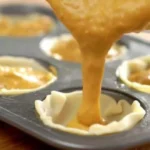 A tray of mini pumpkin pies decorated with whipped cream and spices.