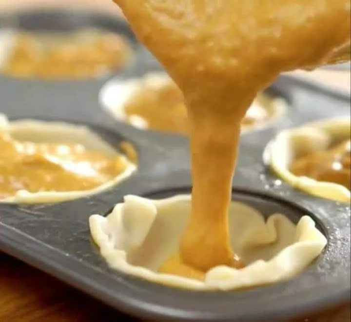 A tray of mini pumpkin pies decorated with whipped cream and spices.