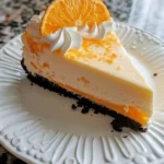 Slice of orange Creamsicle Cheesecake topped with whipped cream and orange zest
