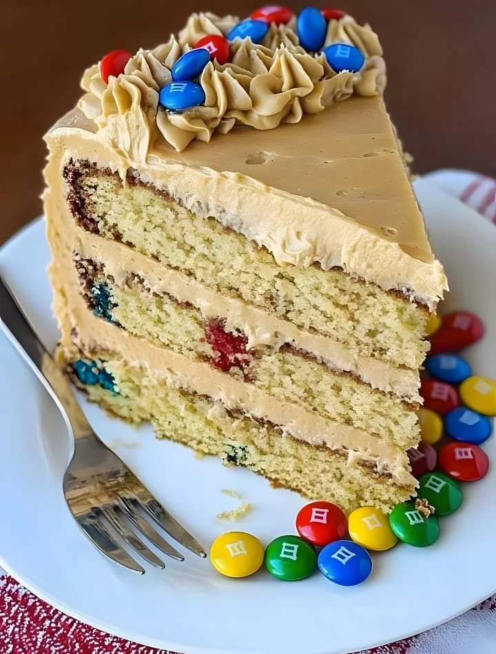 Delicious Peanut Butter M&M Cake topped with colorful M&Ms and creamy frosting.