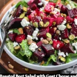 Roasted beet salad topped with goat cheese and pistachios on a white plate.