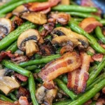 Sautéed green beans with crispy bacon and mushrooms on a white plate