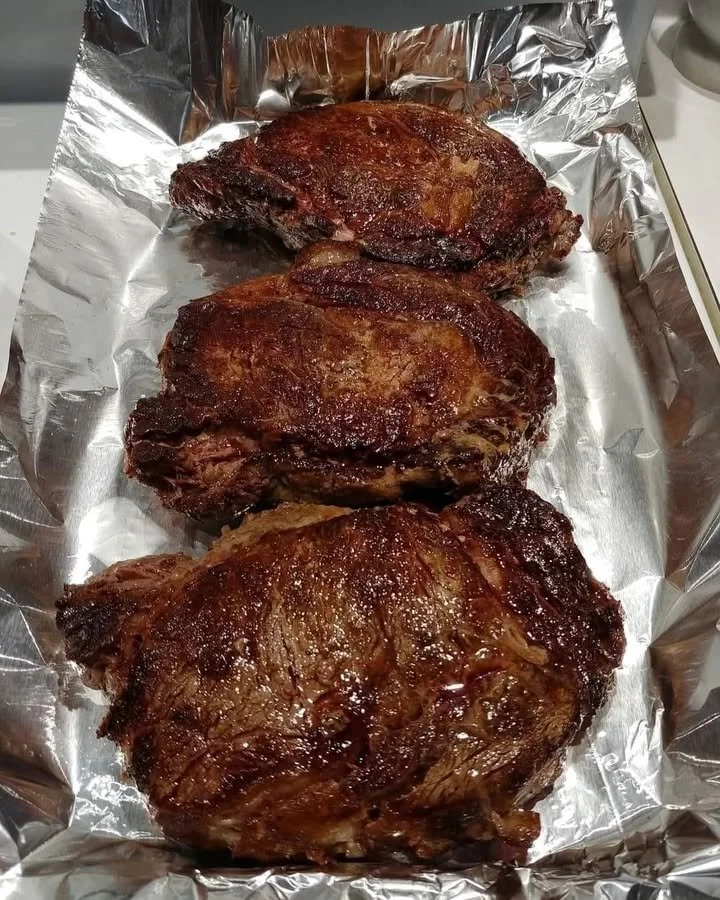 Perfectly seared ribeye steak on a grill, garnished with herbs and spices.