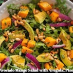 Avocado Mango Salad with arugula, pine nuts, and honey-lime dressing on a plate