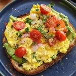 Avocado toast topped with scrambled eggs on a wooden table.