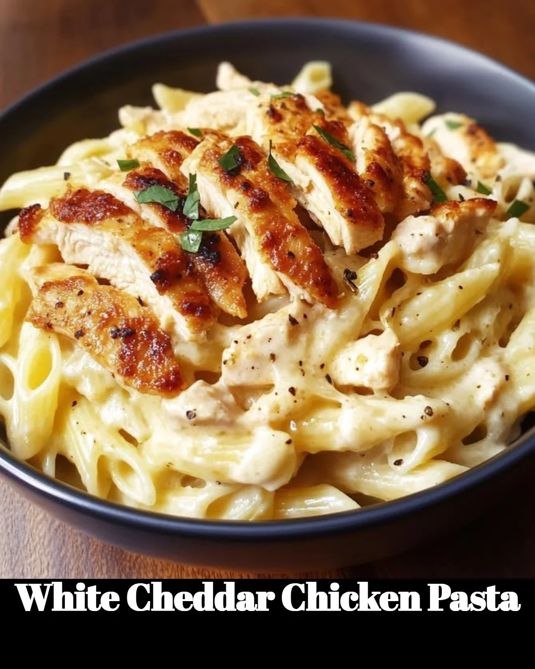Creamy white cheddar chicken pasta dish garnished with herbs and served in a bowl.